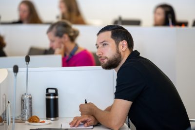 a white man with dark hair and beard looks to the left