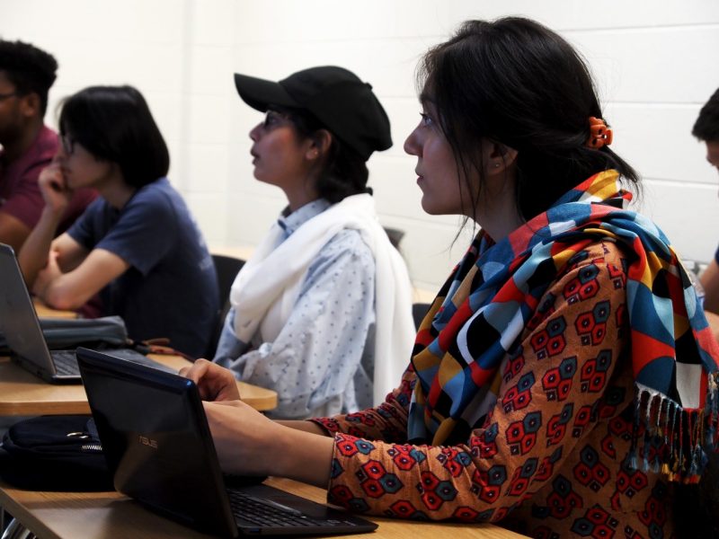 Seated behind their laptops, two female students listen to a presentation. 