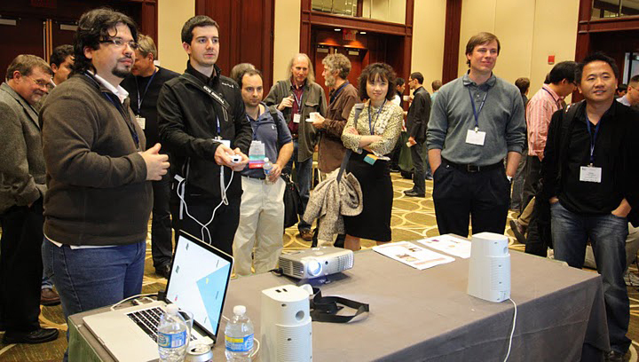 Foreground left, Felipe Bacim stands by as a user tries out the 3-D user interface program for the 2010 Institute of Electrical and Electronics Engineers (IEEE) Symposium by the Fighting Gobblers, the Virginia Tech College of Engineering's computer science department team. The Gobblers captured first place. Standing second to right is Doug Bowman, associate professor of computer science and faculty adviser on the project.