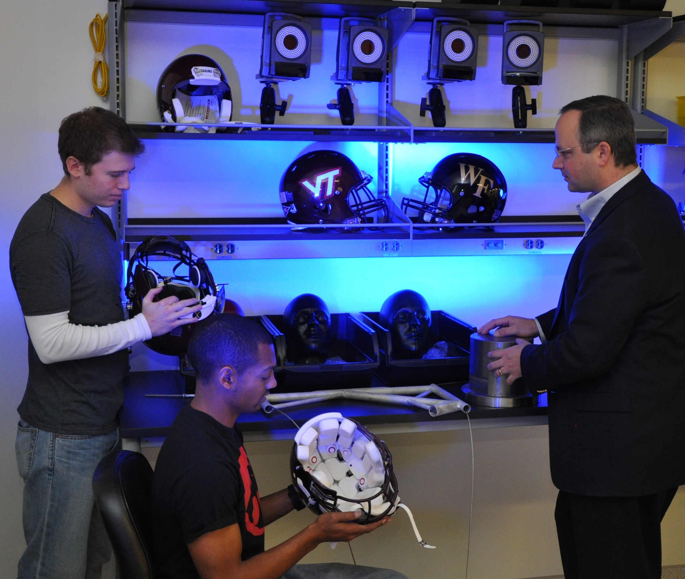 Two professors and a student examine football helmets.