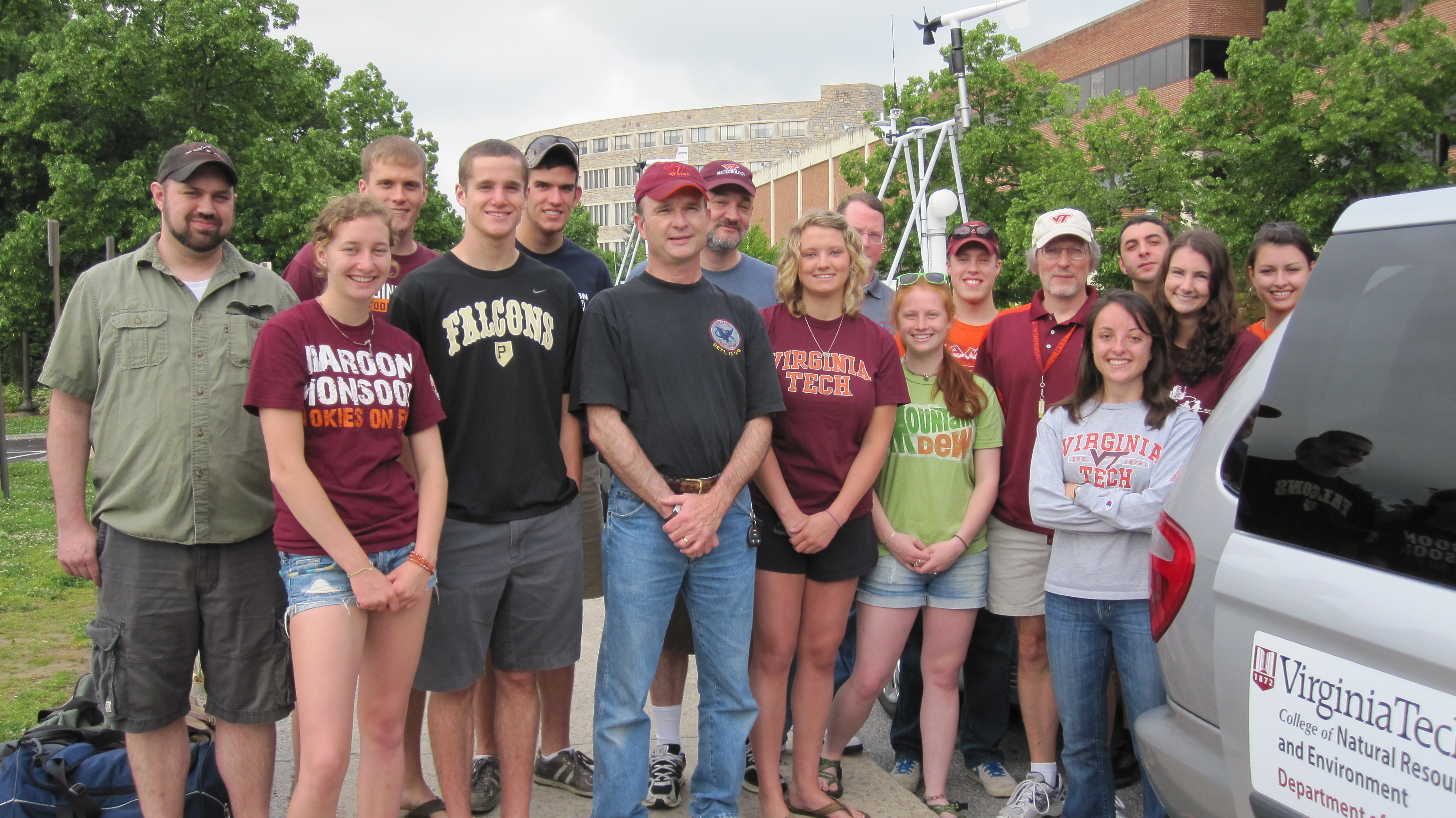 A group of 16 people standing next to a storm chase van.