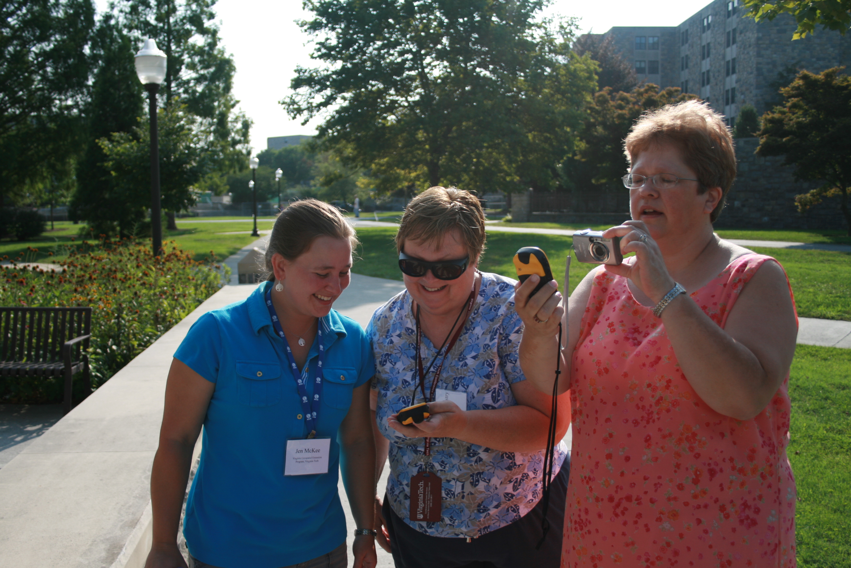 Three women standing outside looking at hand-held GPS devices.