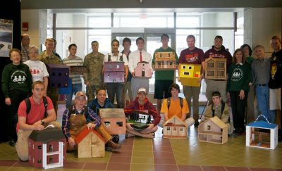 A group of students sitting and standing while holding a variety of different dollhouses.
