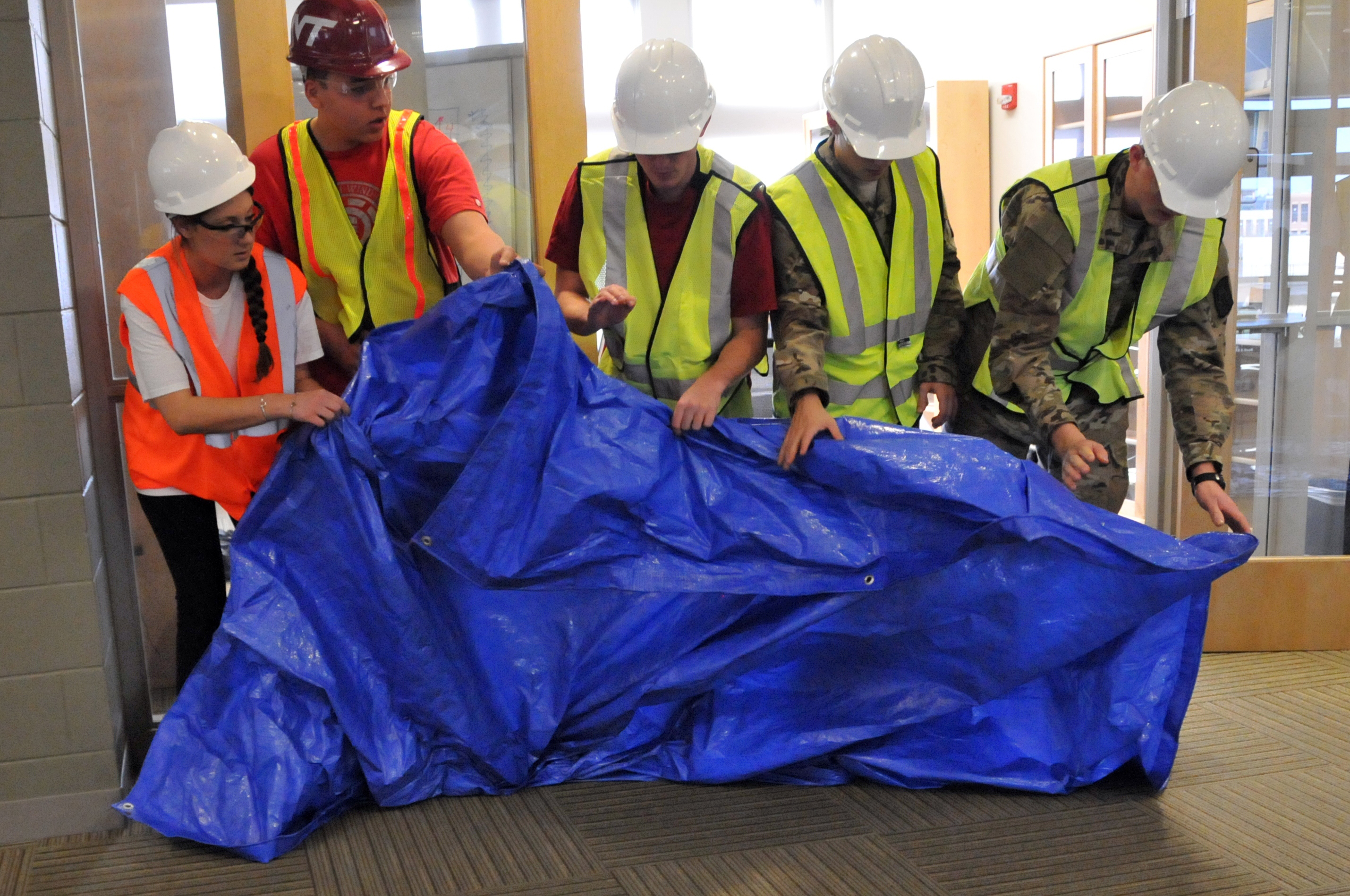 Students in safety helmets and vests working with a tarp.