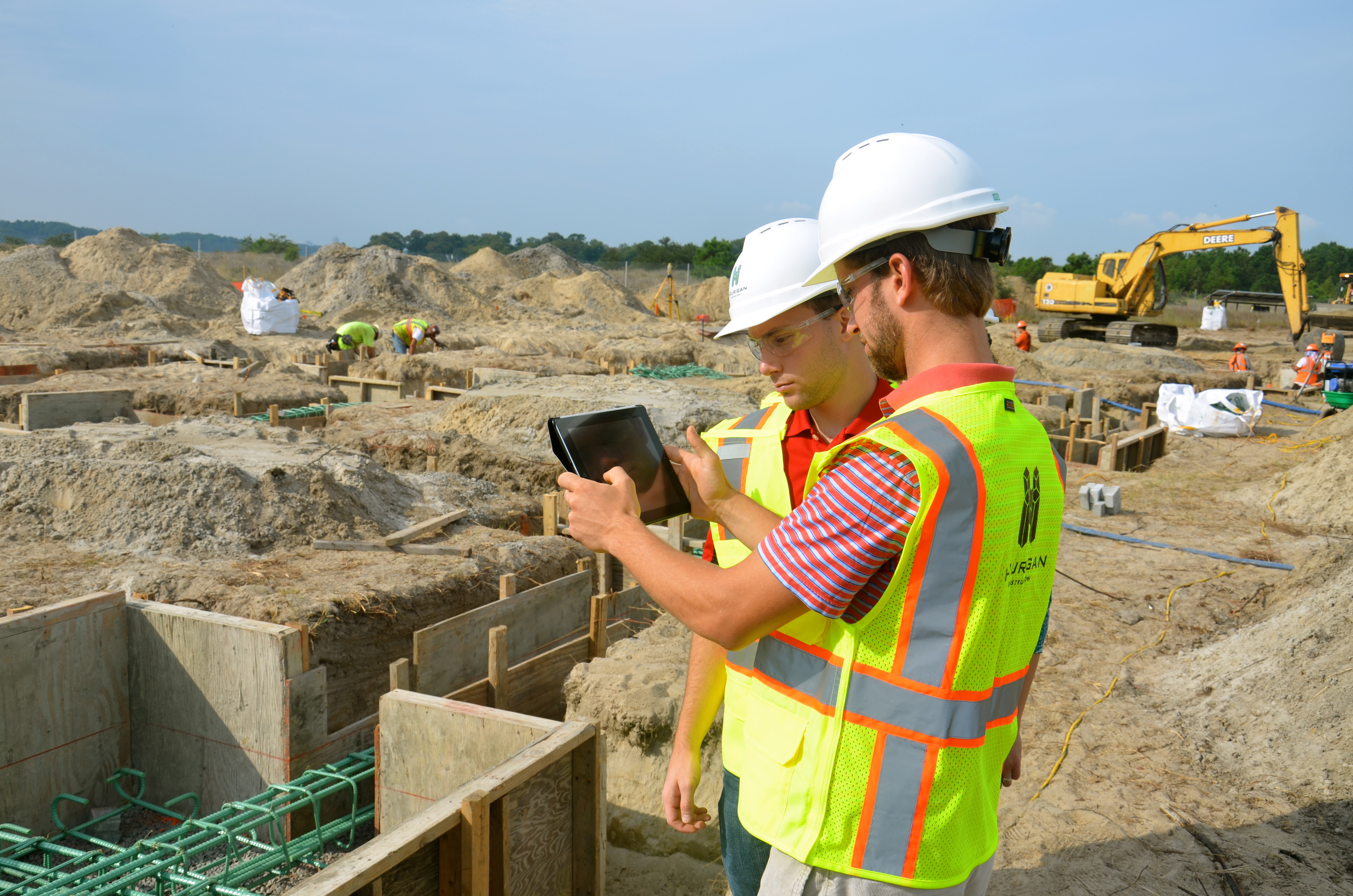 Two students in construction gear survey a building site using an iPad.