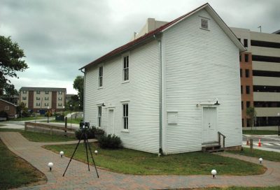 A two story white building with apartments and a parking garage in the background. In the foreground, there are three white spheres on the ground and a scanner on a tripod.