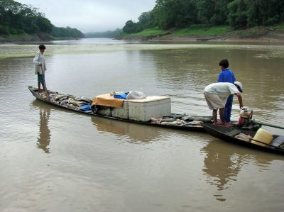 A small wooden boat loaded with fish on a river, with three people aboard