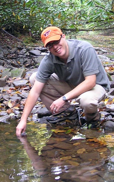 Kevin McGuire takes a water sample in a forest stream