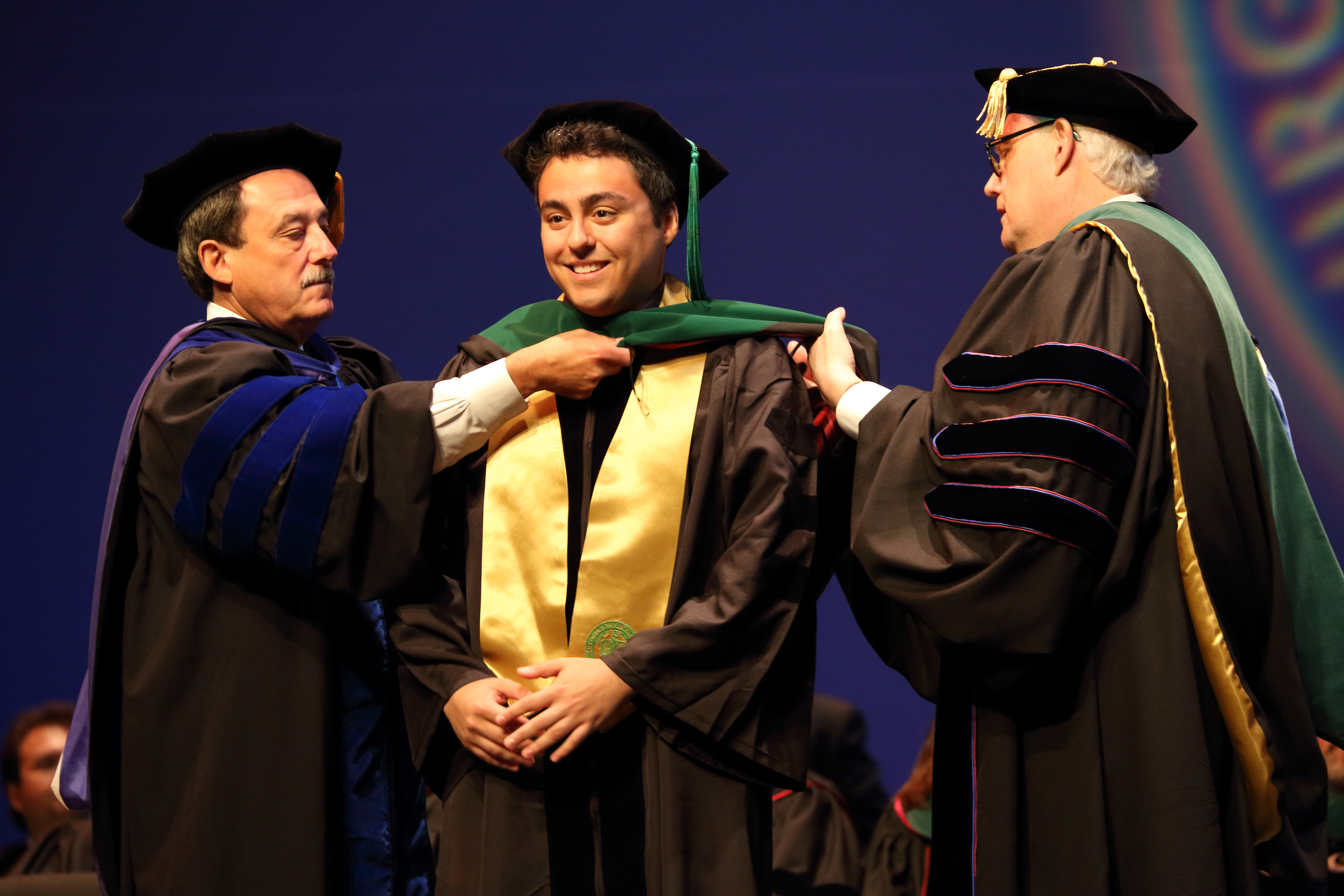 Richard Vari and Daniel Harrington place an academic hood on newly minted doctor Shervin Mirshahi as part of the first-ever graduation of the Virgina Tech Carilion School of Medicine.