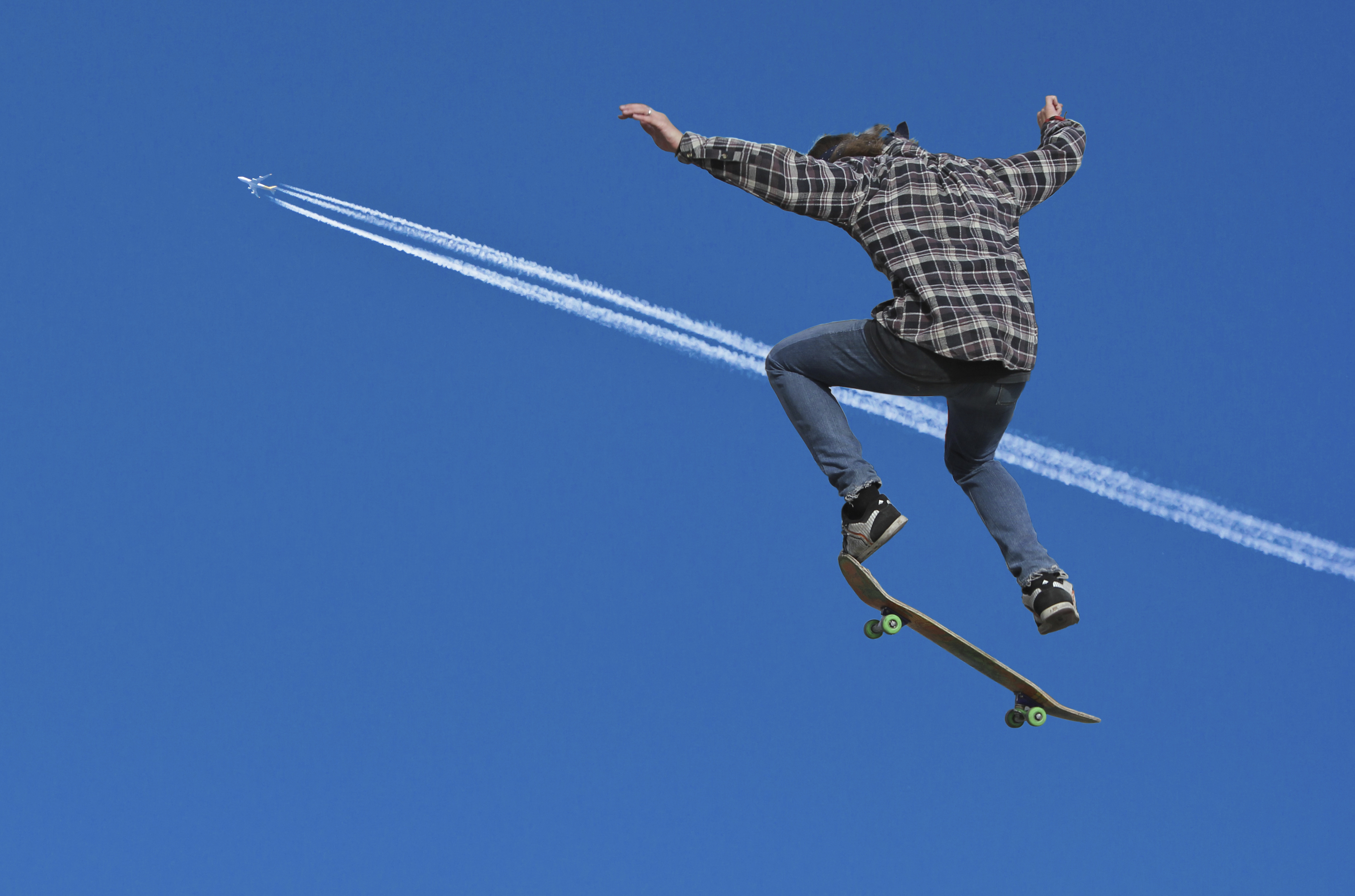 A teenager skateboards with the contrails of a jet in the background