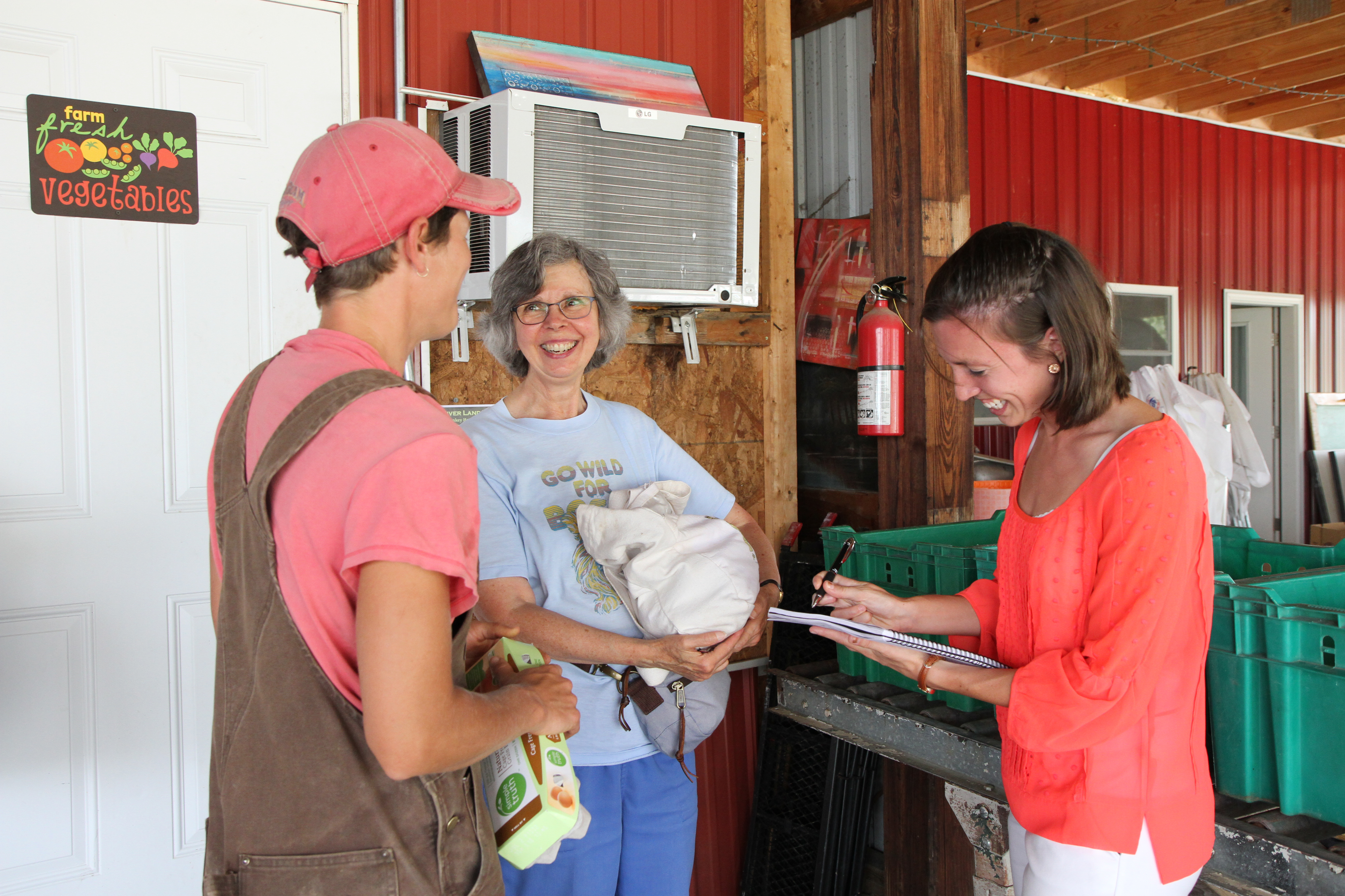 Student holds clipboard as she talks to community member receiving bag of food at local farm.