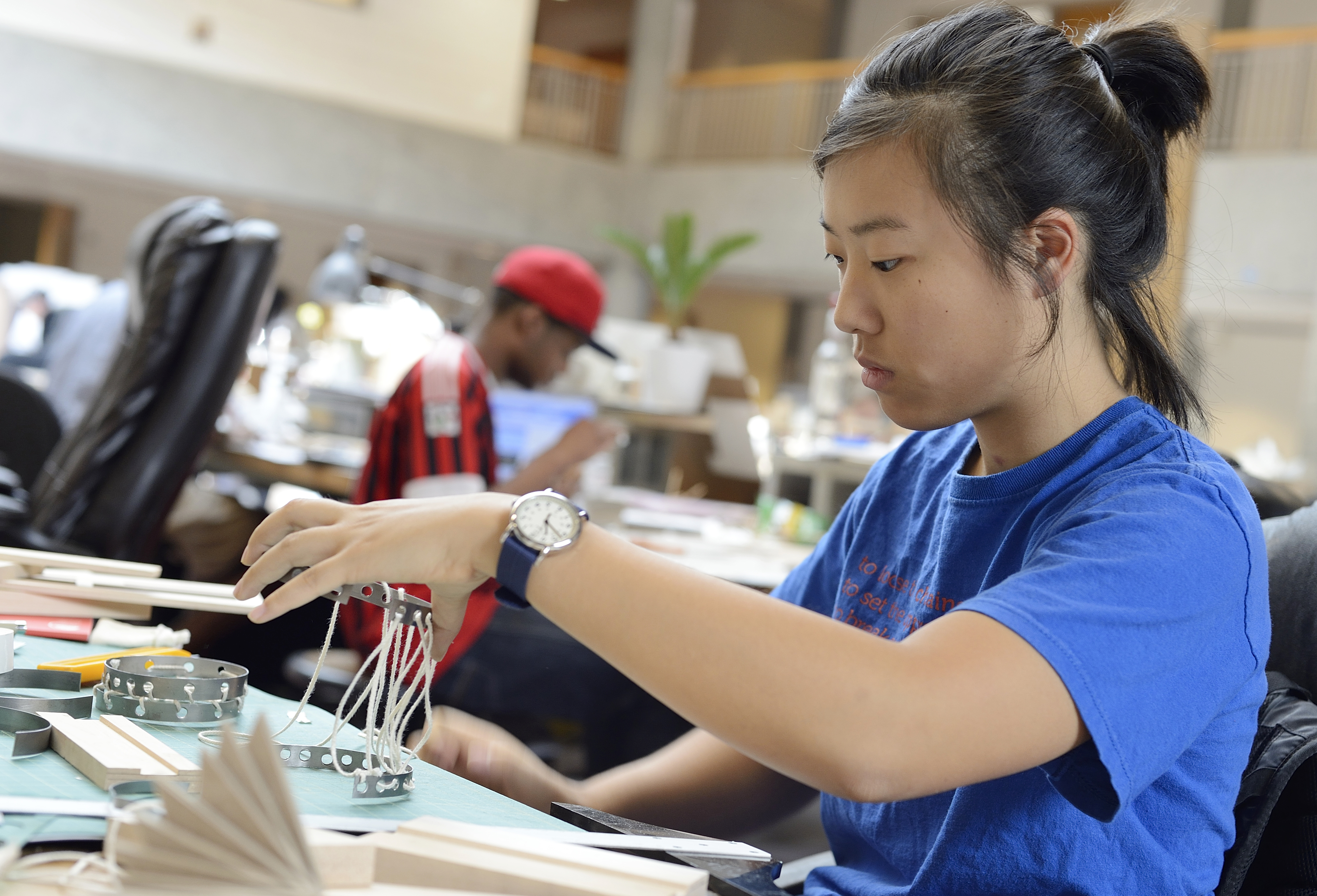 A girl in the foreground works on a design project made of metal and string. 