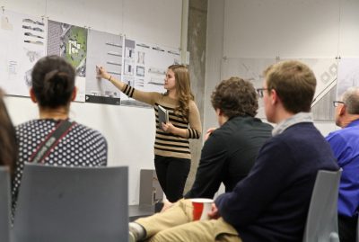 A young woman presents a design board to an audience. 