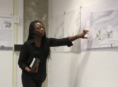 A young woman presents a design board to an audience. 