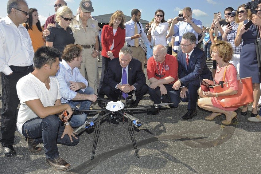 Gov. Terry McAuliffe (third from left) and Virginia Tech President Timothy D. Sands (fifth from left) inspect a Flirtey hexacopter before its flight carrying medicines from the Lonesome Pine Airport to the Wise County Fairgrounds on Friday, July 17, 2015. Researchers were investigating the potential of unmanned aircraft for the delivery of pharmaceuticals and medical supplies in rural areas. Flirtey co-founders (from left) Tom Bass and Matt Sweeney, McAuliffe, Wise County Clerk of Circuit Court Jack  Kennedy, Sands, and Virginia  Secretary of Technology Karen Jackson witnessed the groundbreaking flights.