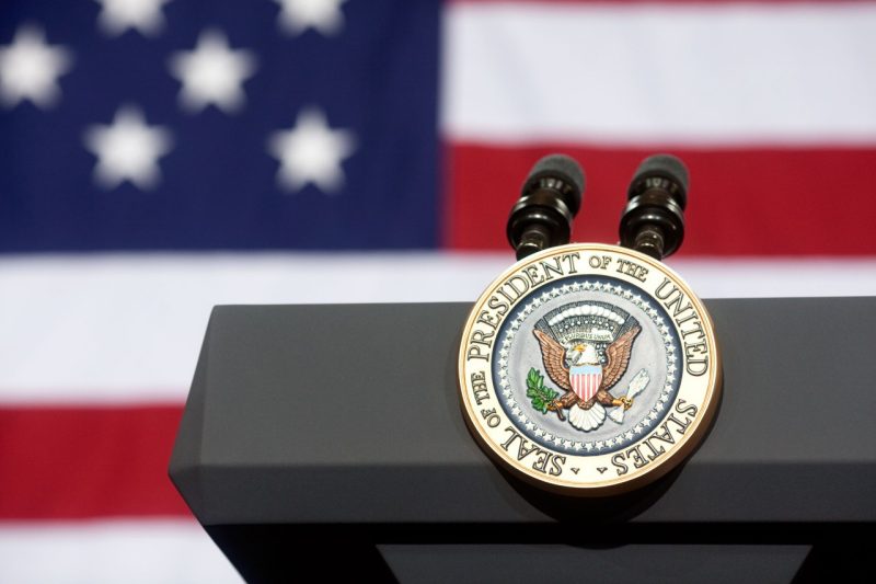 Podium with two microphones and President of the United States seal, flanked by American flag