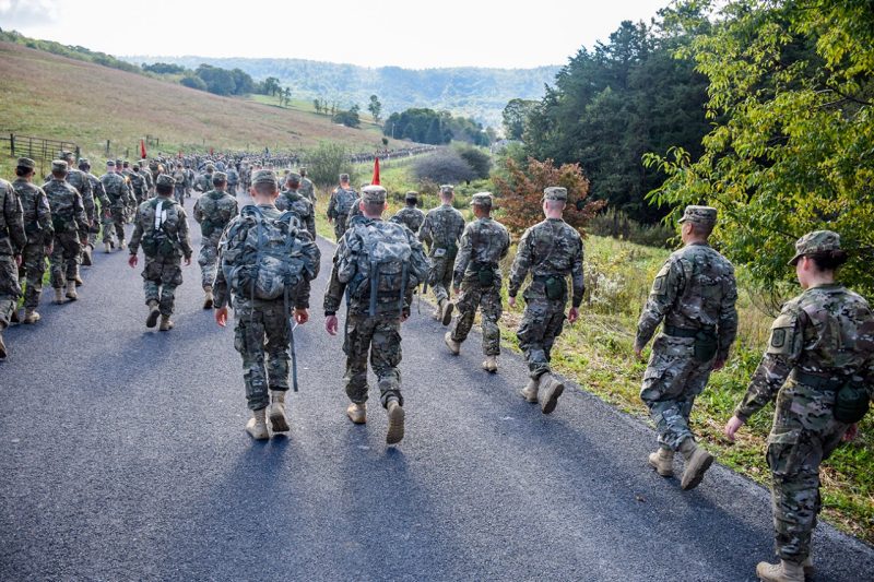 A long column of cadets walks down a rural roadway.