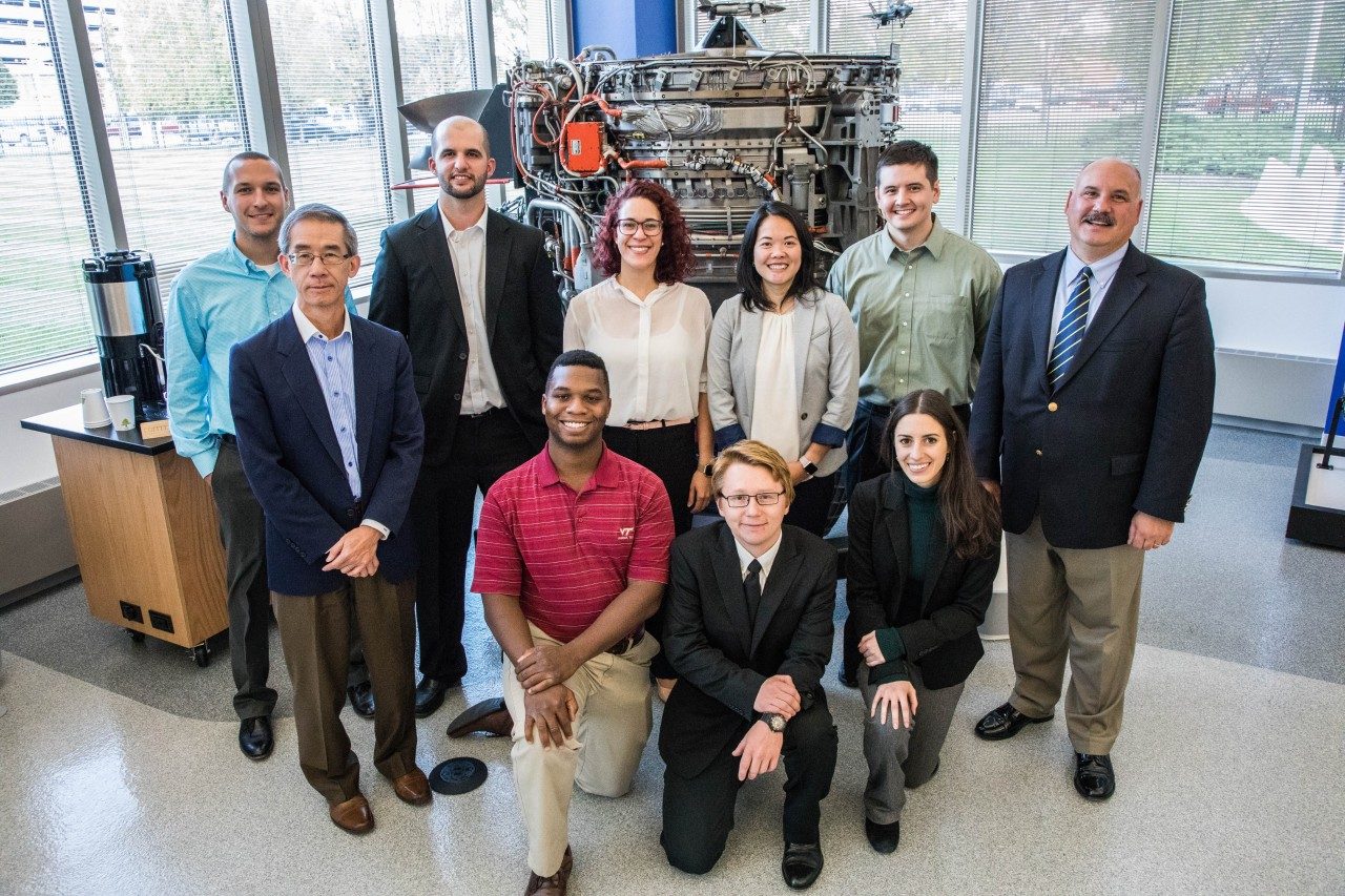 The Virginia Tech students and advisors who work with Rolls-Royce as part of the company's University Technology Center program pose in front of an engine on the Rolls-Royce Indianapolis, Indiana, campus.