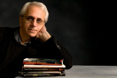 Male professor poses with elbow on stack of books