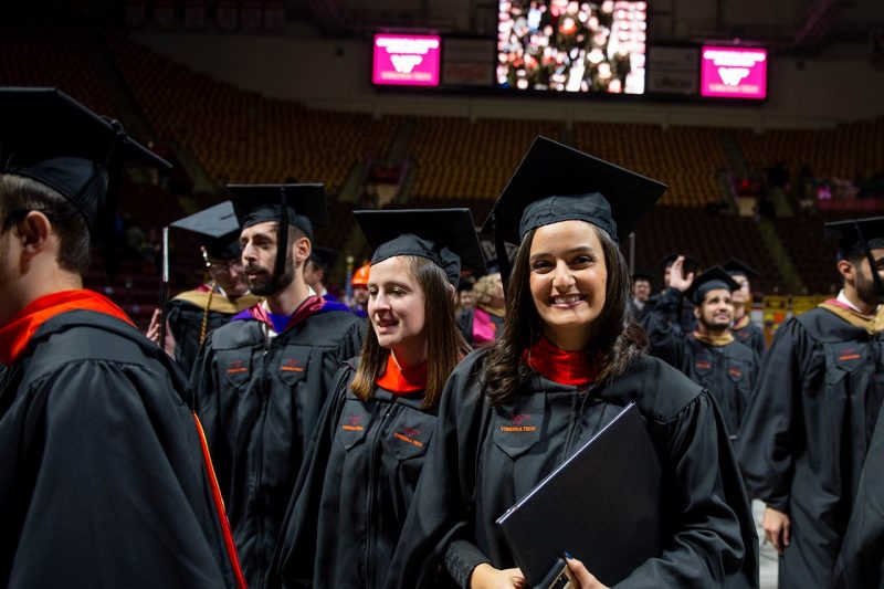 Newly conferred Virginia Tech graduates wearing black caps and gowns with orange embellishments leave Cassell Coliseum during 2018 fall commencement exercises. 