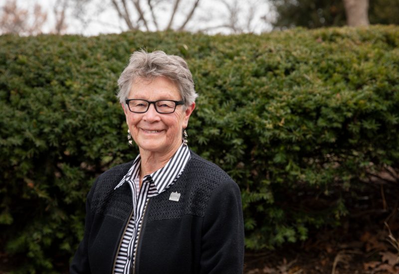photo of Graduate School Dean Karen DePauw standing near shrubs in Arlington VA wearing a striped shirt and a black jacket