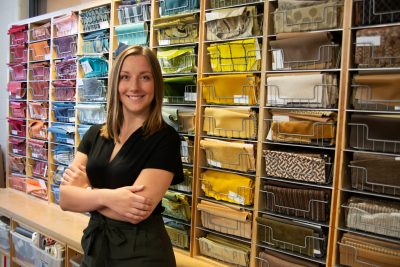 Sydney Miller poses in front of a selection of multi-colored paper designs