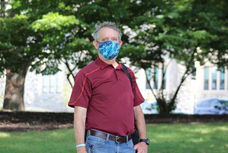 A man wearing a face covering standing outside with trees in the background