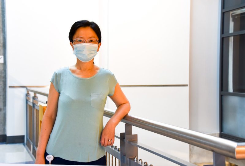 Lini Ni, an assistant professor of neuroscience, poses for a photo in a research building on the Virginia Tech campus. She is wearing a light blue shirt and COVID-standard mask.