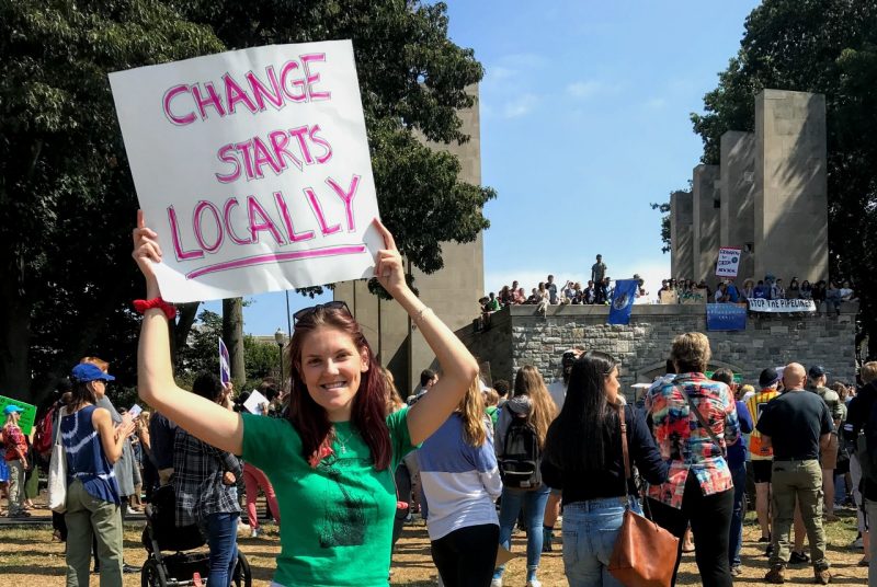 Virginia Tech alumna Natalie Koppier holds sign saying "Change starts locally" during a sustainability rally on campus.
