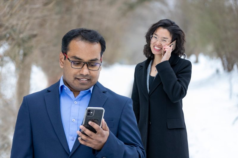 Two researchers on their mobile devices on a walking trail in the snow.