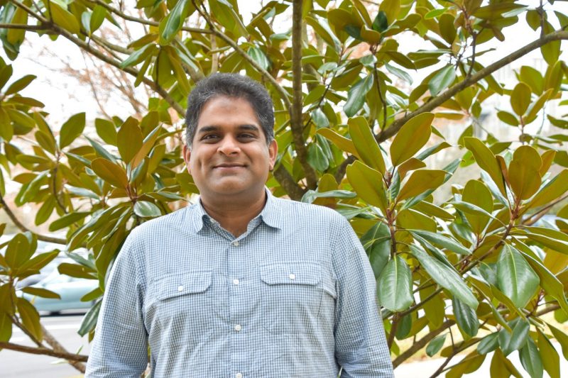 Sujith Vijayan, wearing a dress shirt, stands in front of a small tree.