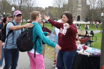 Hokie mom Dayna Fladhammer opens her arms wide to a Virginia Tech student with a backpack as other students look on