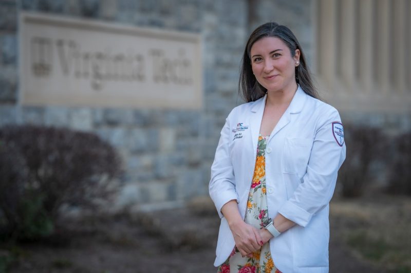 Neslihan Ari wearin her white coat stands in front of the Virginia Tech Carilion School of Medicine.