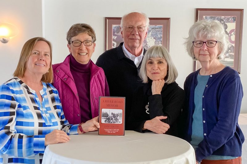 Five people gather around a high round table supporting a book.
