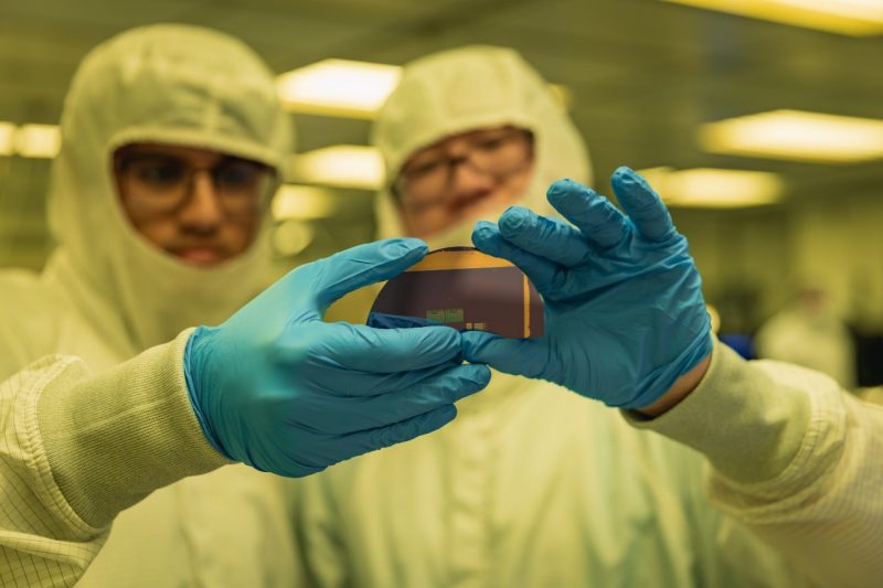 People dressed in clean lab gear holding up semiconductor part
