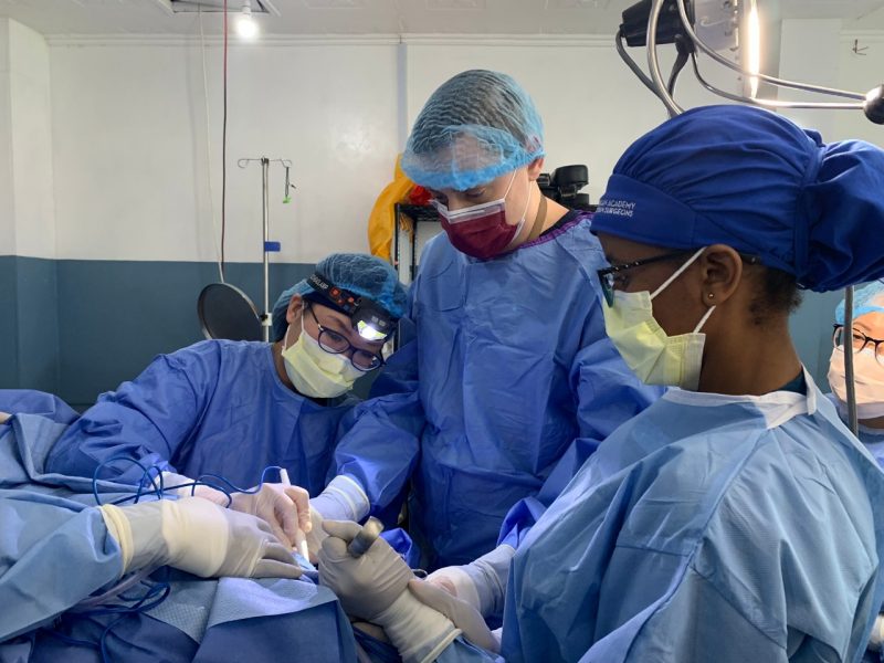 Joanna Kam and Robert Summey wear scrubs and masks while performing a surgery in an operating room in Kenya.