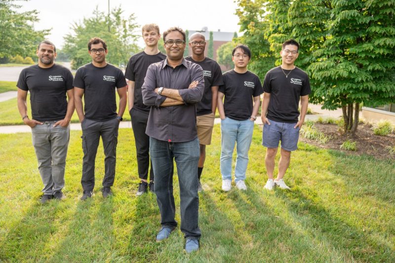 Binoy Ravindran (at front center) stands outside of the Virginia Tech Corporate Research Center with the Software Systems Research Group, including (from left) David Narvaez, Md Syadus Sefat, Nico Naus, Binoy Ravindran (front row), Dale Walker, Yue Yu, and Jae-Won Jang. 