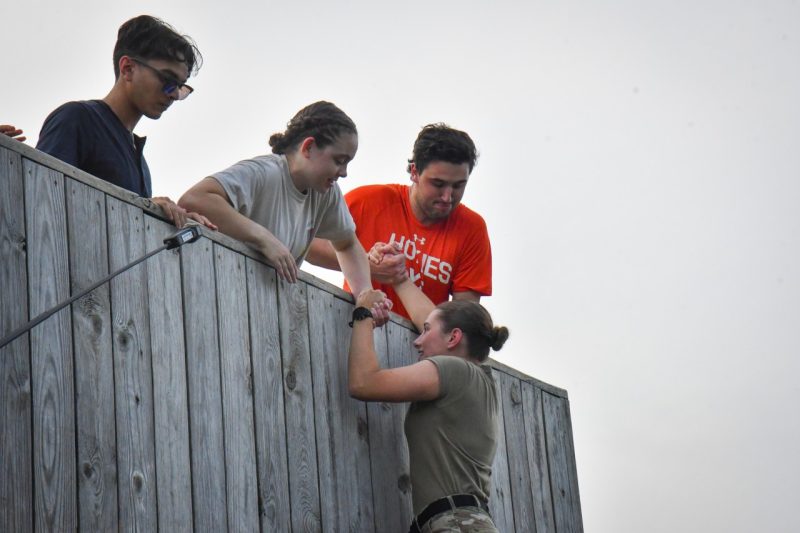 People helping a person climb up a wall. 