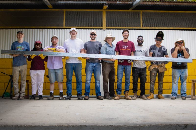 Seven Virginia Tech students, one professor and two Costa Rican hold metal beam with signatures on Costa Rican community center job site.