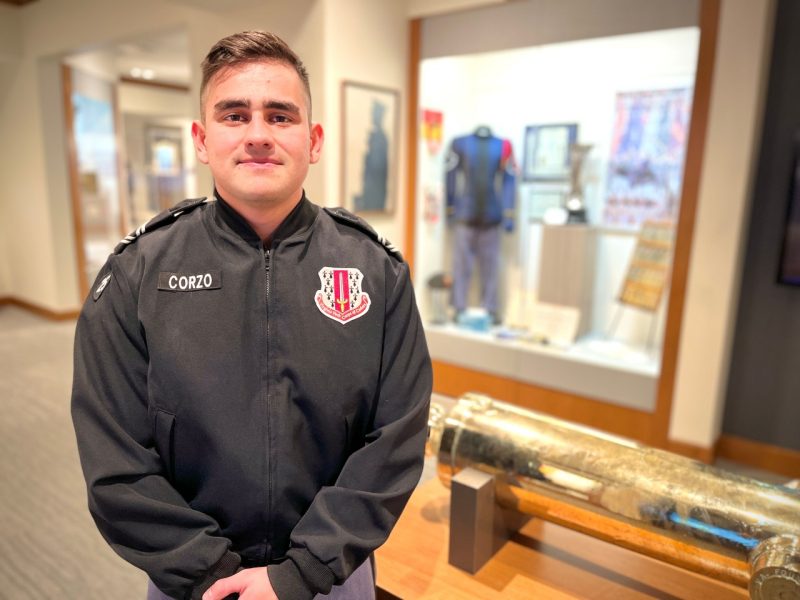 Cadet Corzo stands in his uniform amidst exhibits in the corps museum.