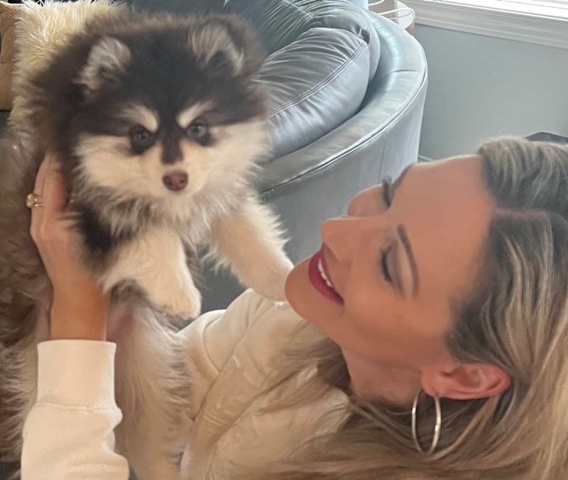 Woman smiles as she looks at fluffy puppy.