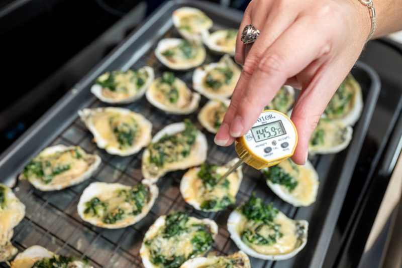 Person holds a food safety thermometer to check the internal temperature of cooked oysters.