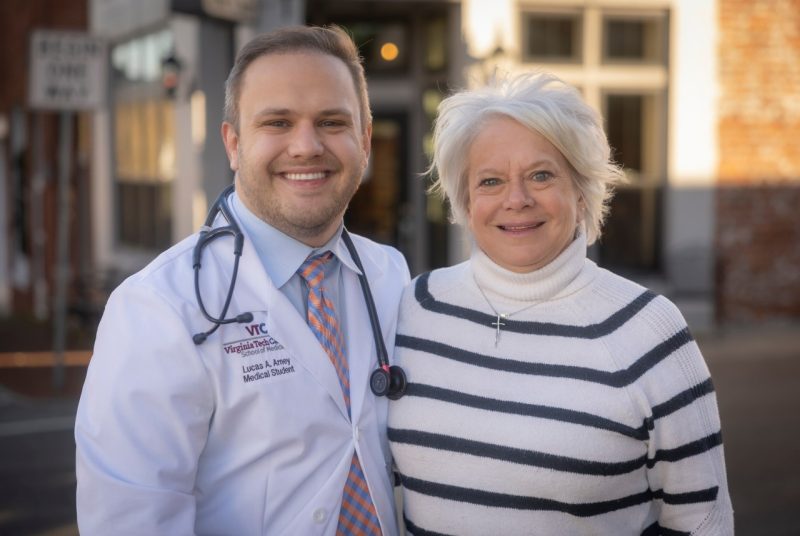 Man wearing doctor's white coat and stethescope standing beside woman outdoors