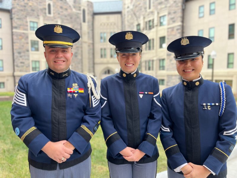 All three cadets stand in front of a Hokie Stone building in their dress uniforms. They are all smiling at the camera. 