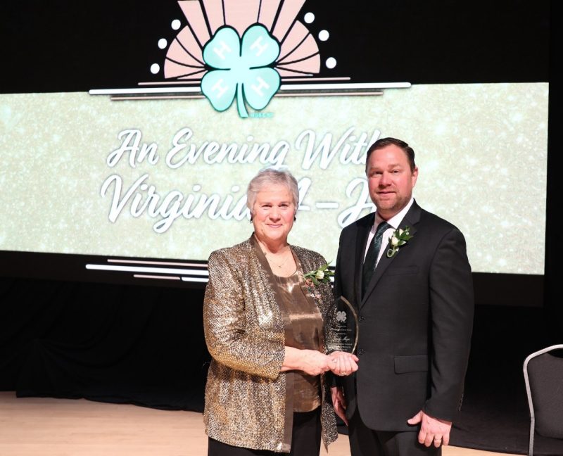 A woman stand stands posed beside a man, holding a glass award, in front of a sign that says, "An Evening with Virginia 4-H."