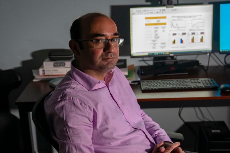 Navid Ghaffarzadegan sitting at his desk in front of COVID-19 data models. 