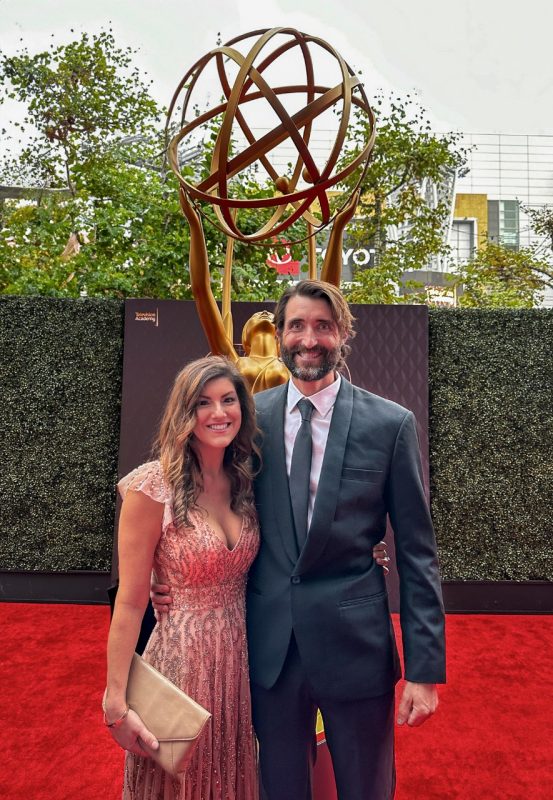 Man in a black suit standing next to a woman in a pink dress at the Emmys.