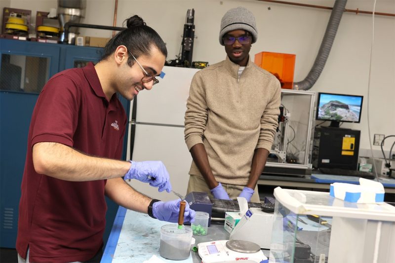 Farideddin Bazzal (at left) prepares a syringe with feedstock for 3D printing of fuel grains for a rocket motor with aerospace engineering senior Giovanni Morris (at right) in the DREAMS Laboratory. 