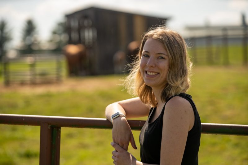 Young woman standing by horse barn outside.
