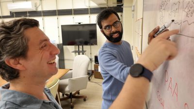 Two physicists work on a problem at a whiteboard.